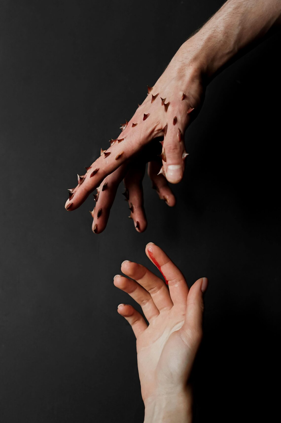 Thorned hand reaching for innocent hand that is bleeding